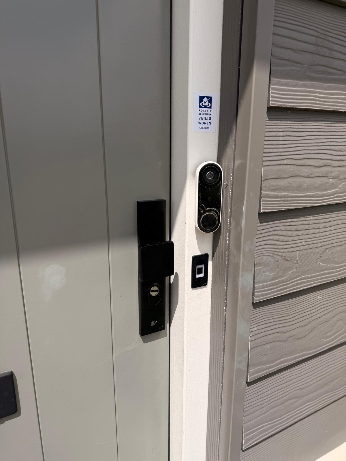 Elektronische bediening en zwart beslag bij een witte voordeur