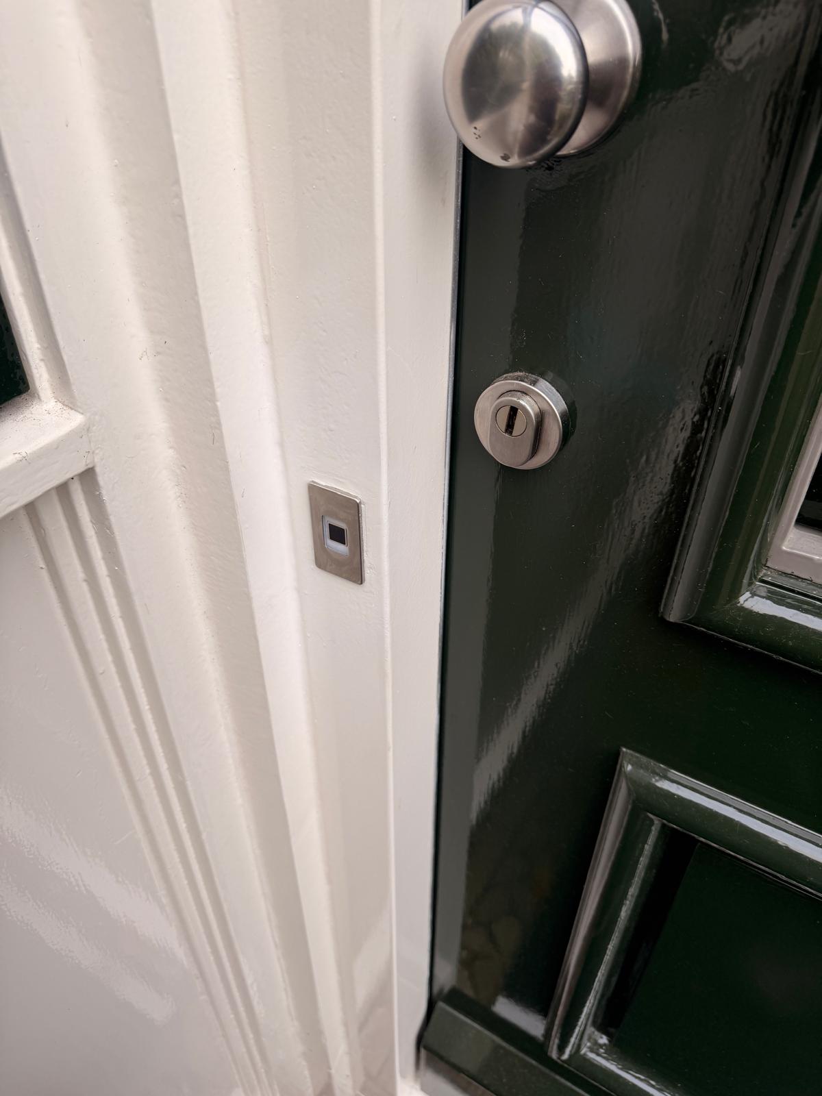 Vingerafdruklezer in een wit kozijn naast een groene deur